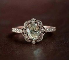 an engagement ring with a large green diamond surrounded by small white diamonds on a black surface