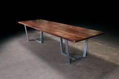 a wooden table sitting on top of a cement floor next to a black wall with metal legs