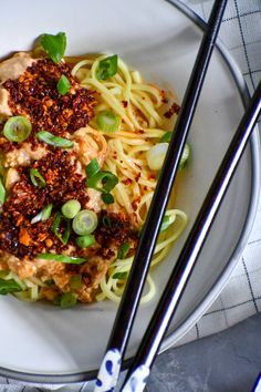 a white plate topped with noodles and meat next to chopsticks on a table