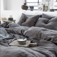 an unmade bed with grey linens and pillows