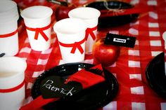 a table topped with black plates covered in red and white napkins next to cups