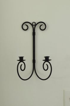 a wall mounted candle holder in the shape of a hook with two candles on it