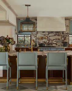 a kitchen with marble counter tops and blue chairs in front of an island that has gold trim