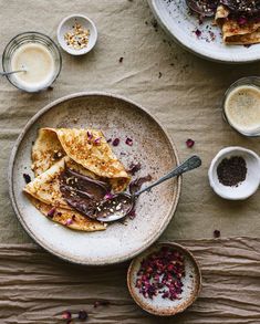 two plates with desserts on them next to cups of coffee and spoons sitting on a table