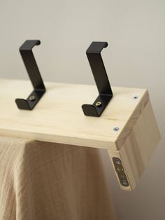 two black metal brackets on top of a wooden table next to a beige cloth covered wall