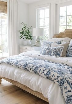 a bed with blue and white comforter in a bedroom next to two large windows