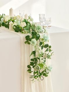 an arrangement of flowers and greenery on a white table cloth draped over the headboard