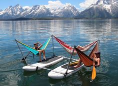 two people sitting in hammock boats on the water with mountains in the background