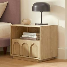 a nightstand with books and a lamp on it in a bedroom area next to a bed