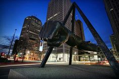 a large metal sculpture in the middle of a city at night with buildings behind it