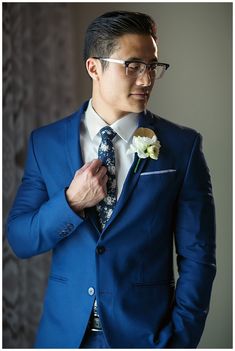 a man in a blue suit adjusts his floral boutonniere on his lapel