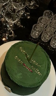 there is a green cake on the table with wine glasses in the backround