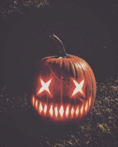 a carved pumpkin sitting in the grass with its eyes open and two glowing stars on it's face