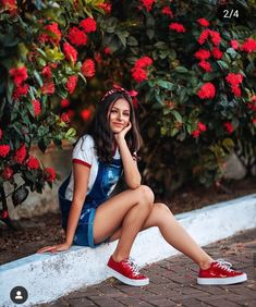 a woman sitting on a ledge with red flowers in the background and her hand under her chin