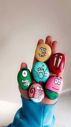 someone is holding up some rocks with cartoon characters painted on them in the palm of their hand