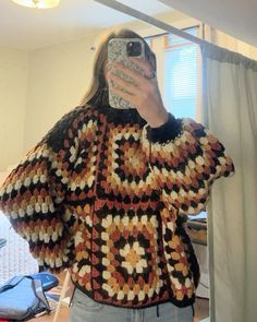 a woman taking a selfie while wearing a crocheted sweater and jeans in front of a mirror