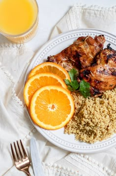 a white plate topped with meat and rice next to orange slices on top of a table