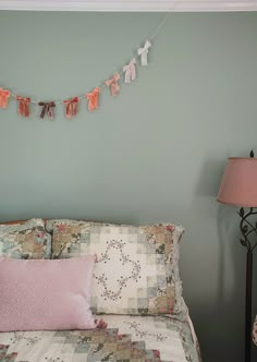 a bed with a quilt and pillows on it in front of a wall hanging clothes