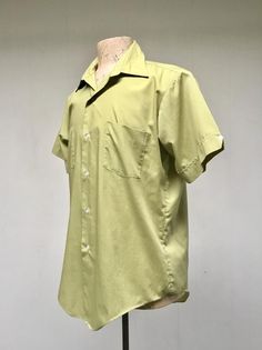 * Men's casual shirt c 1970s* Green polyester-cotton blend fabric * Medium pointed collar* Double chest patch pockets * Short, set-in sleeves with sewn down notched cuff with button detail* Action pleats below back yoke* 6 button front closure* Long tailsLabel: Master Built - Permanent Press - 15 1/2Excellent conditionChest: 44Shoulder: 18Sleeve: 9Length: 31 (center back)Garments are flat-measured. Please compare these measurements to another flat-measured garment that fits you correctly for siz Relaxed Fit Cotton Camp Shirt With Collar, Fitted Cotton Camp Shirt With Spread Collar, Fitted Cotton Shirt With Camp Collar, Retro Cotton Collared Camp Shirt, Vintage Camp Shirt With Pockets And Relaxed Fit, Fitted Green Collared Camp Shirt, Retro Shirt With Johnny Collar And Relaxed Fit, Green Cotton Short Sleeve Shirt With Spread Collar, Retro Collared Short Sleeve Shirt Relaxed Fit