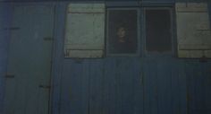 a woman is looking out the window of an old blue building with shutters on it