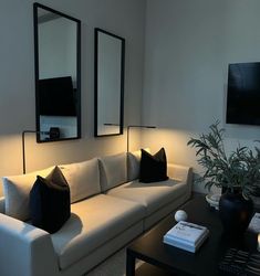 a living room with white couches and two mirrors on the wall, along with a black coffee table