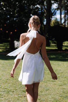 a woman in a white dress is walking through the grass with her back to the camera