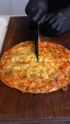 a person cutting into a pizza on top of a wooden board with a knife in it