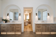 a bathroom with double sinks and two mirrors on the wall, along with an arched doorway leading to another room