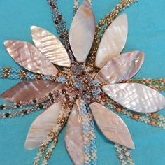 a flower made out of shells and beads on a blue tablecloth with beaded trimmings