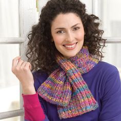 a woman with curly hair wearing a multicolored knitted scarf and smiling at the camera