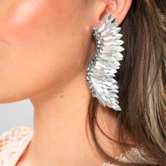 The Silver Statement Wing Earrings are the perfect accessory for those who want to make a bold statement with their jewelry. The wings symbolize freedom and lightness, and these earrings capture that essence in their unique design. The handmade sequins shimmer in the light, catching the eye and adding a touch of glamour to any outfit. These silver wing earrings are perfect for any occasion, from a night out with friends to a formal event. Add these stunning earrings to your collection and elevat Handmade Silver Wrap Earrings For Party, Trendy Silver Bling Earrings, Metal Wrap Drop Earrings For Party, Silver Single Crystal Earring For Party, Metal Wrap Earrings For Party, Silver Pierced Wrap Earrings For Party, Silver Pierced Crystal Earrings For Party, Elegant Silver Winged Earrings, Trendy Pierced Wrap Earrings For Party