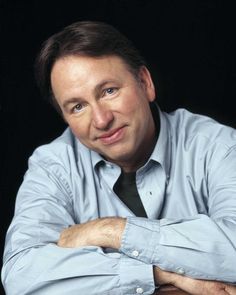 a man wearing a blue shirt and black tie posing for a photo with his arms crossed