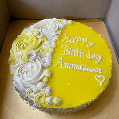 a yellow birthday cake with white frosting and flowers on it sitting in a box