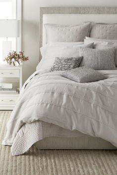 a bed with white linens and pillows in a neutral bedroom, next to a window