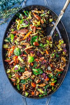 a skillet filled with vegetables and rice on top of a blue tablecloth next to a spoon