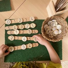 a child is playing with wooden numbers and counting them on a green mat next to a wicker basket