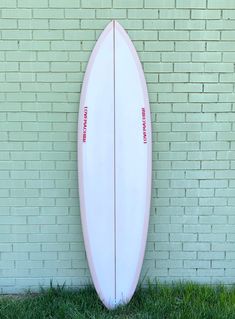 a white surfboard leaning against a brick wall in front of a green grass lawn