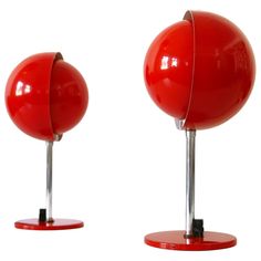 two red balls are sitting on metal bases, one is turned upside down and the other is slightly open