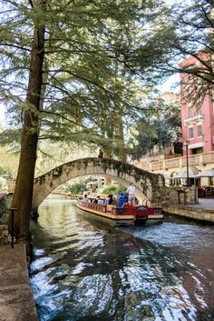 people are riding in a boat on the water under a bridge over a small river