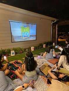 group of people sitting on the grass in front of a large screen watching an outdoor movie