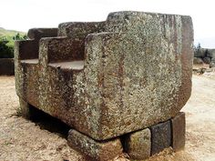 a large stone bench sitting in the middle of a dirt field next to some rocks