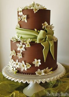 a three tiered chocolate cake with white flowers on the side and green ribbon around the top