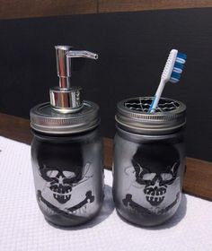 two mason jars with skull and crossbones painted on them, one has a toothbrush in it