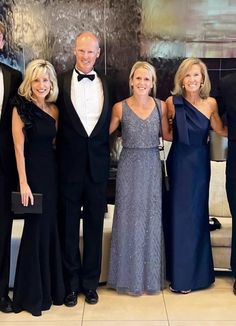 a group of people standing next to each other in formal wear and tuxedos