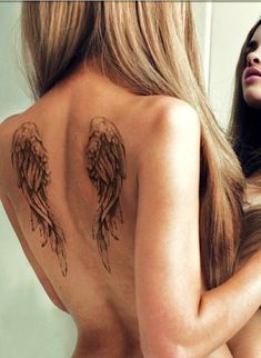 the back of a woman's body with angel wings tattoo on her upper half