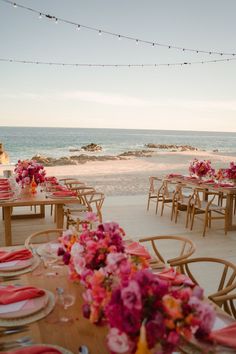 tables set up on the beach with pink flowers and place settings in front of the ocean