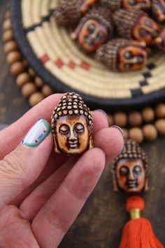 a hand holding a small ceramic buddha figurine in front of some beads on a table