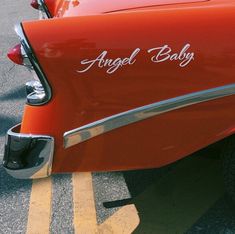 an orange car with the word angel baby written on it's tail end is parked in a parking lot