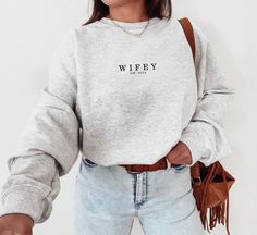 Minimalistic Wifey Sweatshirt 💖 | Custom Wifey Crewneck Celebrate your love with our cozy Wifey Sweatshirt! Perfect for newlyweds, this custom crewneck makes a great engagement or honeymoon gift. SIZE UP 2 SIZES FOR OVERSIZED LOOK PRODUCTION TIME: 1-3 business days SHIPPING TIME: 2-7 business days SIZING AND COLOR: * Please check the images for sizing details. * Please check the images for color options. CARE INSTRUCTION: Wash inside out, in cold water, on gentle cycle. Tumble dry low or let air dry. Do not use Fabric Softeners or Bleach Do not dry clean. Avoid ironing on the design.  PRINTING METHOD: DTG printing method is used for these shirts. PRODUCT:  .: Medium-heavy fabric blend of 50% cotton and 50% polyester (8.0 oz/yd² (271.25 g/m .: Classic Fit .: Say goodbye to itchiness thanks Fiance Sweatshirt, Husband Clothes, Wife Sweatshirt, Wifey Sweatshirt, Honeymoon Gift, Custom Crewneck, Honeymoon Gifts, New Wife, Wife Gift