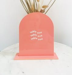 there is a small pink vase with flowers in it on the table next to a white wall